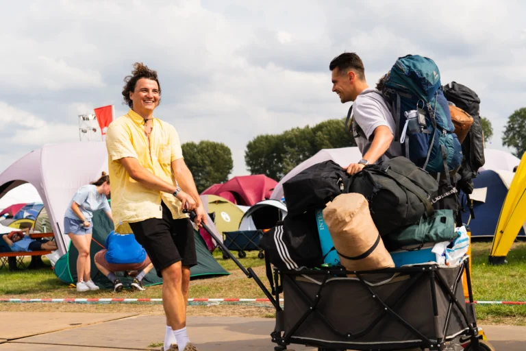 Festival ganger met een berg spullen in een kar lopend over het Lowlands festival terrein.